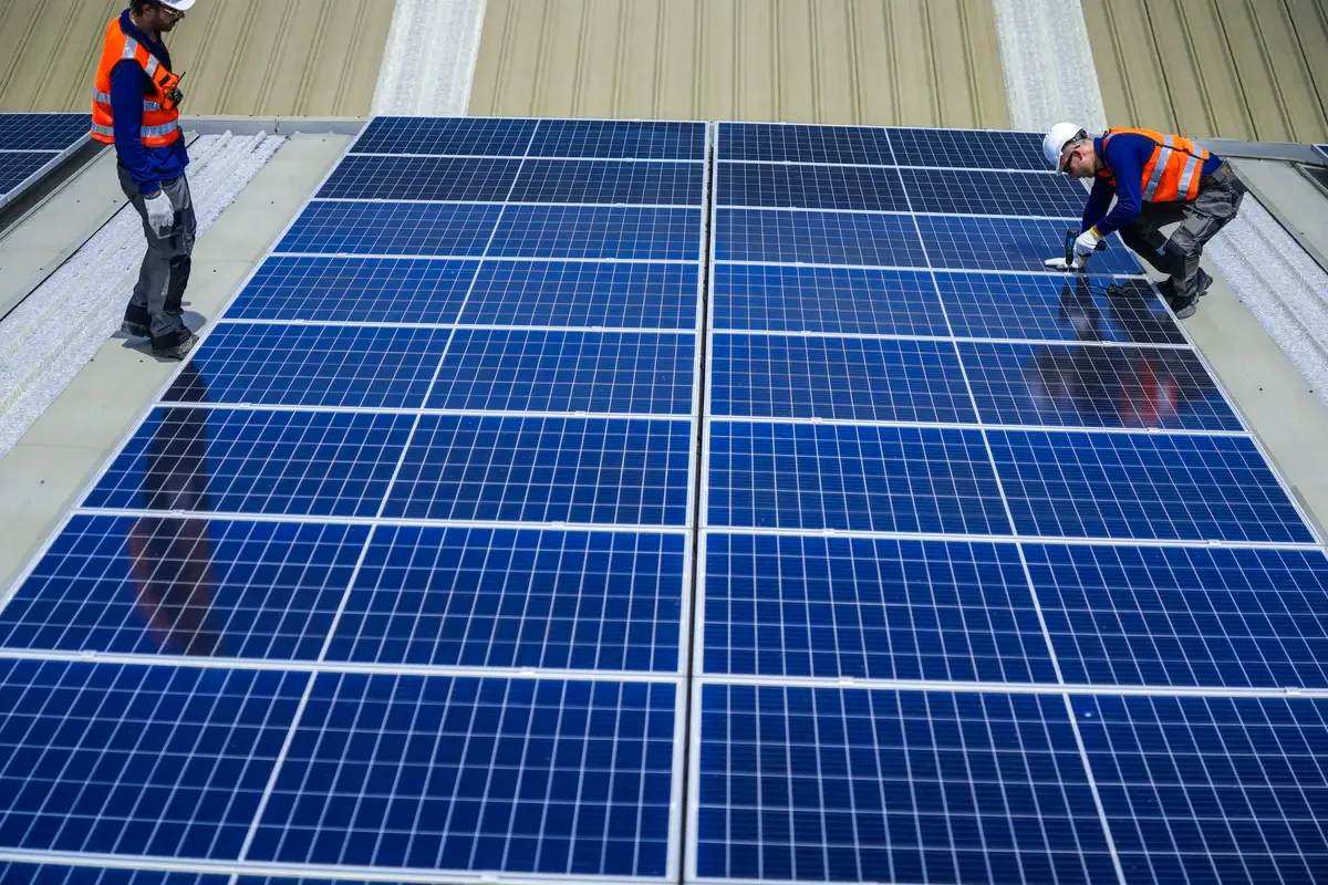 Dos operarios colocando paneles solares sobre la cubierta de una nave de empresa cerca de Badalona